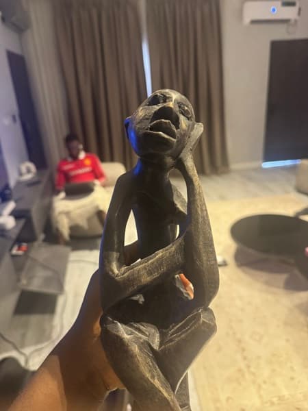 A carved wooden thinker sculpture held in one hand